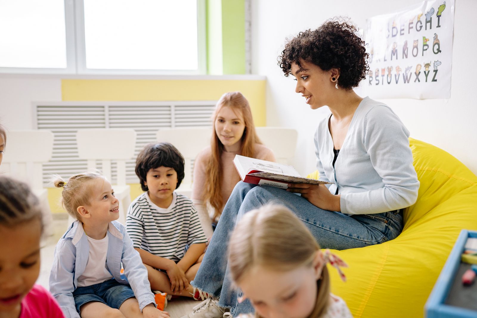 A woman reading a book aloud to a small group of young children seated around her
