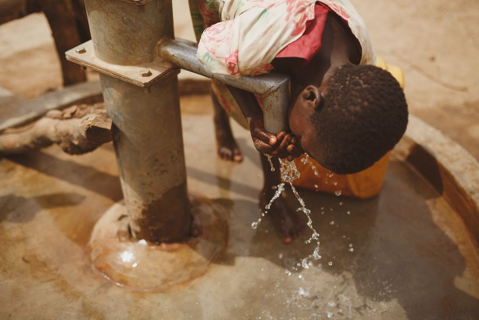 A child bending to drink water flowing from a hand pump