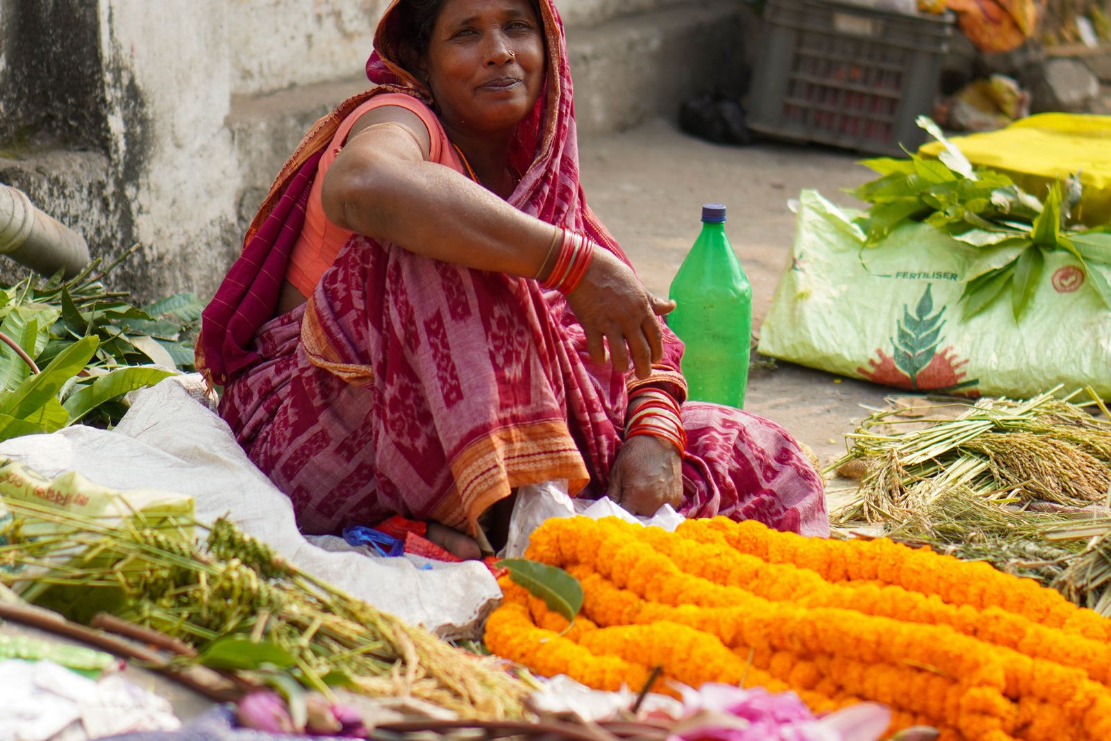 A woman seated at a street stall selling vegetables and marigold flowers
